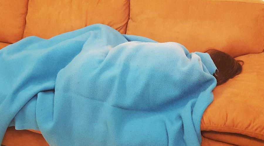 ילדה מכוסה בשמיכה שוכבת על ספה