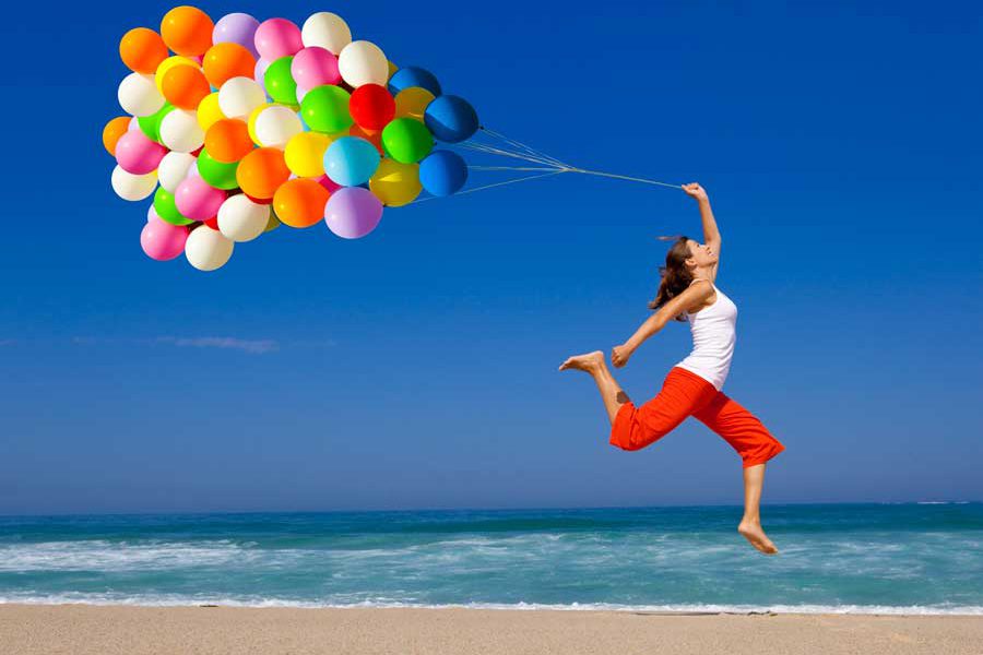 בחורה קופצת בחוף הים מחזיקה ערימת בלונים באוויר