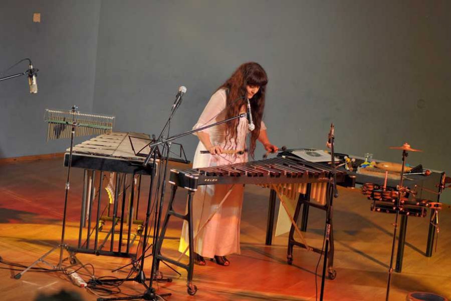 אישה בשמלה לבנה מנגנת על כלי הקשה
