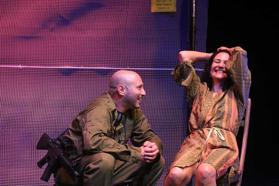 אישה צוחקת יושבת על כיסא וגבר לידה הם על במה