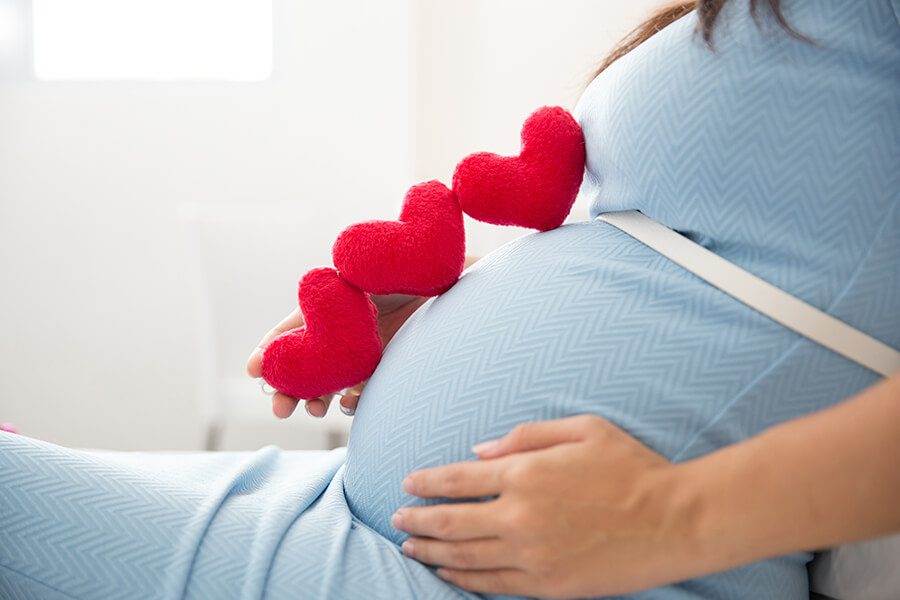 בטן אישה בהריון ושלוש לבבות אדומים עליה