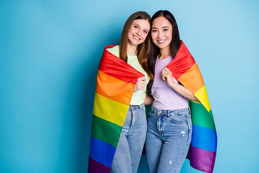שתי בנות מחובקות עטופות בדגל הגאווה