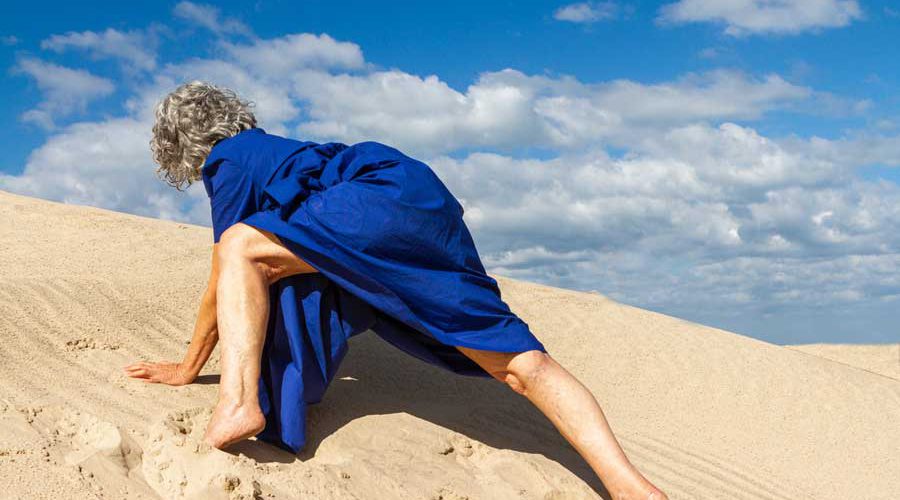 אישה בשמלה כחולה מטפסת על גבעת חול