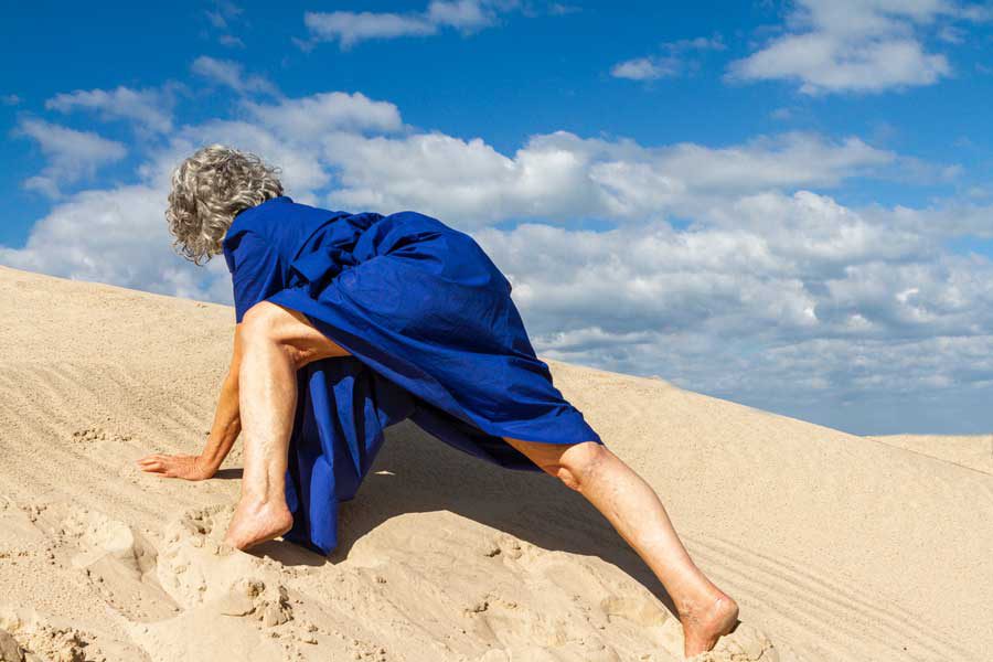אישה בשמלה כחולה מטפסת על גבעת חול