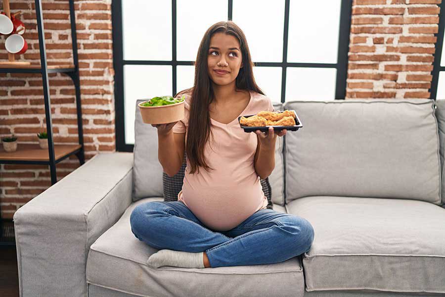 אישה בהריון מחזיקה צלחת אוכל בכל יד