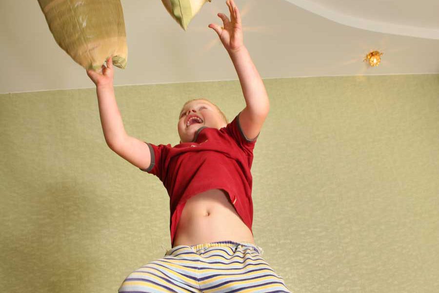 ילד קופץ על מיטה וזורק כריות באוויר